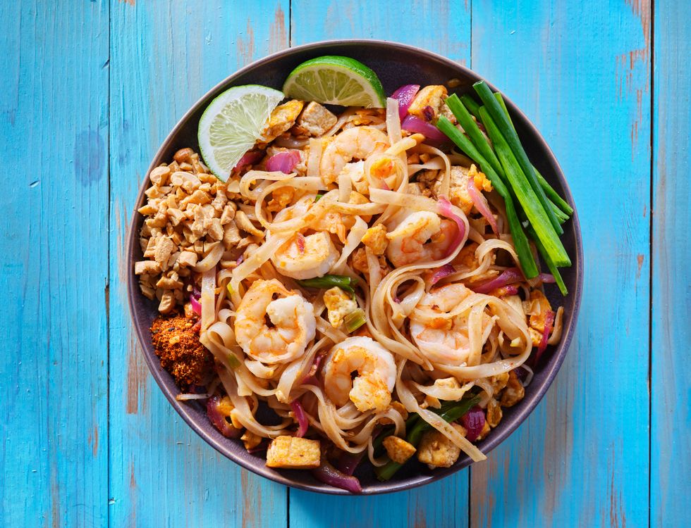 shrimp pad thai on plate in flat lay composition with copy space atop of colorful wooden table